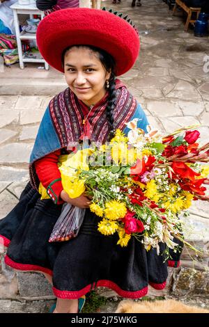 A Portrait Of A Young Indigenous Quechua Woman Holding Flowers At The Sunday Market In The Village Of Chinchero, Cusco Region, Peru. Stock Photo