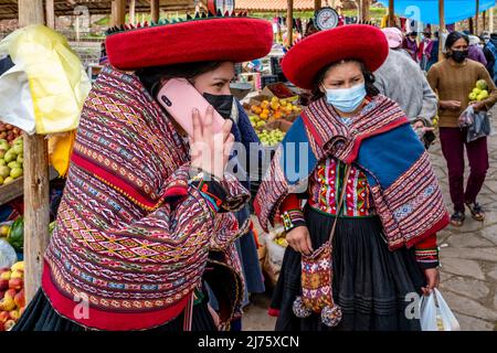 Young Indigenous Quechua Women Using Mobile Phones At The Famous Sunday Market In The Village Of Chinchero, The Sacred Valley, Urubamba Province, Peru Stock Photo