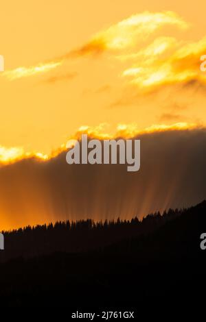 Sun rays in the evening red, break through between cloud and forested mountain. Stock Photo