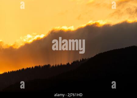 Sun rays in the evening red, break through between cloud and forested mountain. Stock Photo