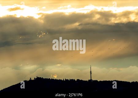 A flock of birds flies over the Hoher Peißenberg near Weilheim in the Bavarian foothills of the Alps during a thunderstorm light atmosphere Stock Photo