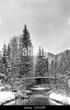 Old stone bridge on the Obernach between Wallgau and Walchensee in winter with thick snow and clouds. The small stream meanders through the winter landscape Stock Photo