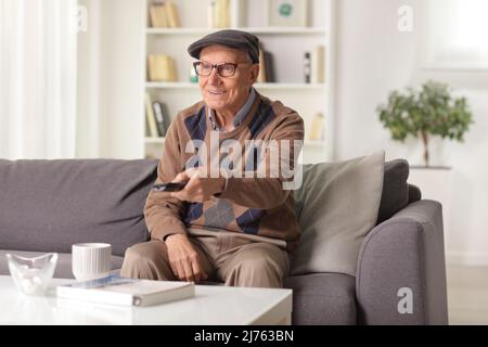 Elderly man sitting on a sofa and holding a remote control Stock Photo