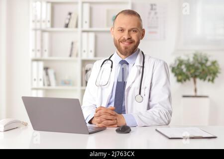 Young male doctor sitting in an office with a laptop computer on the desk Stock Photo