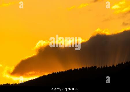 Sun rays in the evening red, break through between cloud and forested mountain. Stock Photo