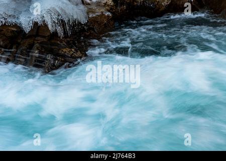 Fast water of the Rissbach forms spray and current. Ice structures and rocks formed on the bank of the mountain stream, border the image. Taken in winter in Tyrol, Austria in the Eng, near the Ahornboden. Stock Photo