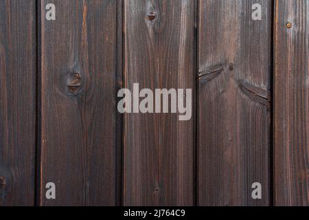 Detailed texture of a dark brown wooden wall with vertical planks. Natural wood surface with visible grain, knots and weathered structure. Stock Photo
