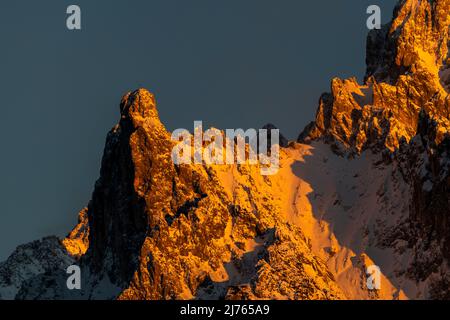 The Viererspitze (2054 m a.s.l.) above Mittenwald, below the western Karwendelspitze, as part of the Northern Karwendel Range in the evening glow of the setting sun in red and orange hues against a blue sky in winter with snow. Stock Photo