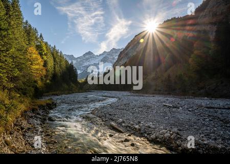 Evening sun in autumn at Johannisbach in Johannistal near Hinterriss in Karwendel, Tyrol / Austria. The mountain stream meanders through its natural gravel bed as the sun sets on the mountain slope, in the background the Laliderer walls with snow. Stock Photo
