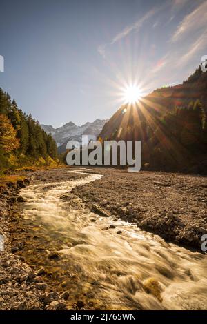 Evening sun in autumn at Johannisbach in Johannistal near Hinterriss in Karwendel, Tyrol / Austria. The mountain stream meanders through its natural gravel bed as the sun sets on the mountain slope, in the background the Laliderer walls with snow. Stock Photo