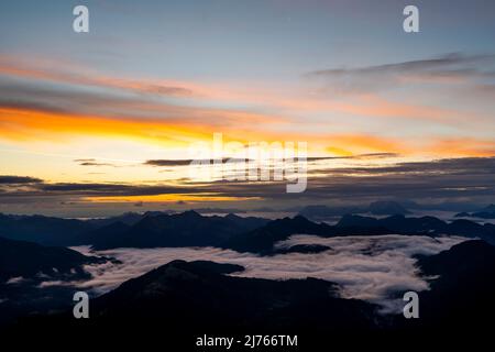 Sunrise with sun star and light colored clouds, while in the valley fog and clouds are moving. View from Guffert (2194m) in Rofan early in the morning. Stock Photo