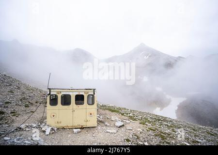 The bivouac box in the Breitgrieskar, in the middle of the inhospitable, moonscape-like landscape of rock and stone in the Karwendel in bad weather, dense clouds and fog. Stock Photo
