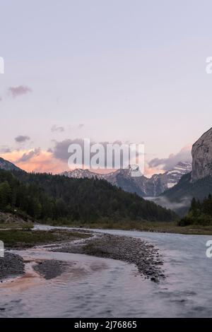 Lightly colored clouds and the flowing water at the Rissbach in the Karwendel Nature Park just before the Großer Ahornboden. In the foreground the stream, in the background mountain and sunset light. Stock Photo