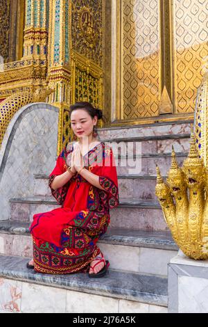 Young woman prays and has her picture taken by tourists, Royal Palace, Grand Palace, Wat Phra Kaeo, Temple of the Emerald Buddha, Bangkok, Thailand, Asia