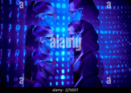 Side view of young virtual people in flashing LED goggles standing against binary code Stock Photo