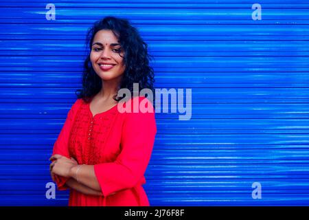 Attractive beautiful happy young latin hispanic woman with teak bindi on forehead smiling on blue wall street background Stock Photo