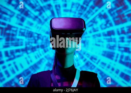 Serious young woman immersed into augmented reality using virtual reality simulator against digital background Stock Photo