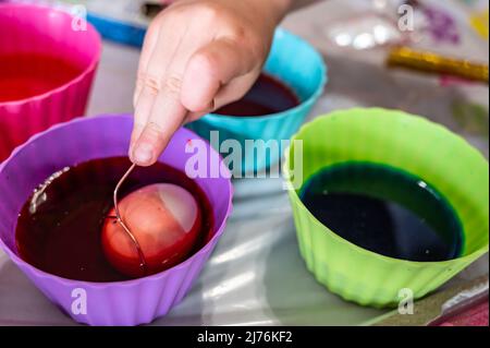 Cups of dye with an egg being lowered in for Easter decorations Stock Photo