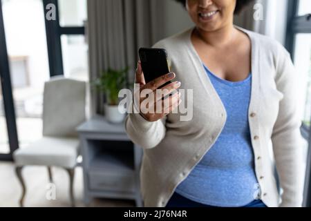 Midsection of smiling mid adult woman using smart phone while standing at home Stock Photo