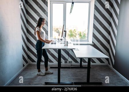 Standing Workplace. Working in Standing Position. Standing desk for work from home or in office. Young woman programmer working while standing in Stock Photo