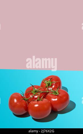 A bunch of fresh tomatoes on a pink-blue background. Hard light, deep shadow. Close-up, copy space. Stock Photo