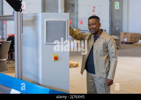 Portrait of smiling african american young male worker standing by machinery in warehouse Stock Photo