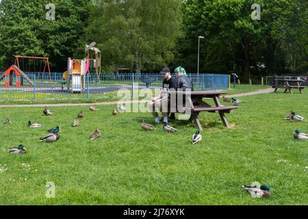 Young couple sitting in a park feeding the ducks Stock Photo