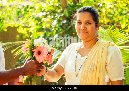 indian man holding bouquet and making surprise for his wife outdoor in park Stock Photo