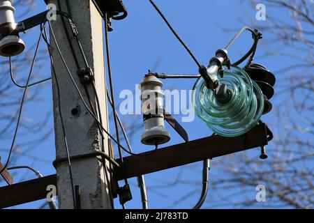 Close-up of high-voltage power lines and power pylons against a blue sky. Stock Photo