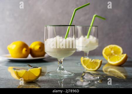 Lemon sorbet in two glasses with lemons, ice cubes and drinking straws on grey background Stock Photo