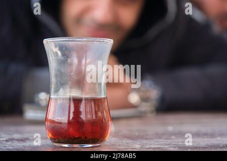 Traditional turkish tea inside traditional slim waisted glass cup, blurred smiley man photo behind the tea glass. Stock Photo