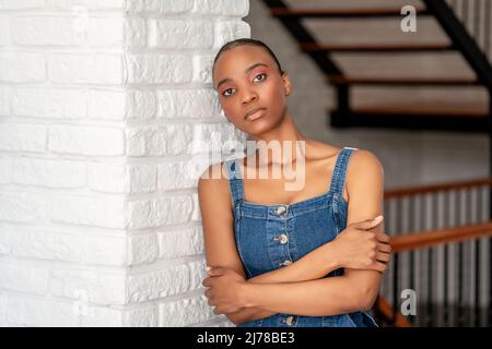 Young dark skin woman leans back on a white brick wall with crossed arms and looking to a point. High quality photo Stock Photo
