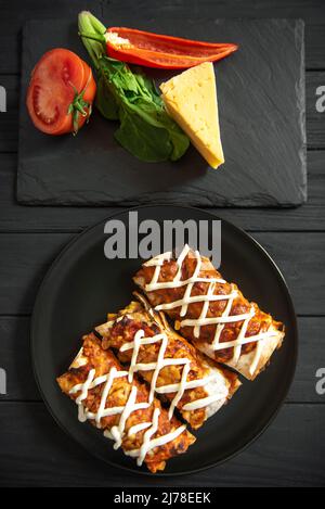 Cooked enchiladas on a black plate on a dark background. Top view Stock Photo