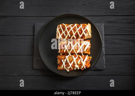 Cooked enchiladas on a black plate on a dark background. Top view Stock Photo