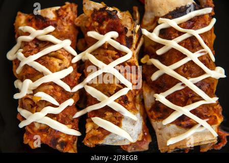 Cooked enchiladas on a black plate on a dark background. Top view close up Stock Photo