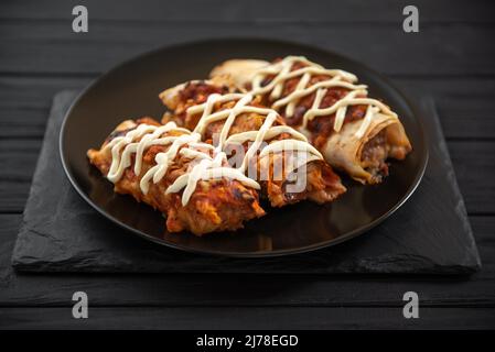 Cooked enchiladas on a black plate on a dark background. Stock Photo