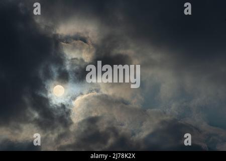 Photograph of full Moon between heavy clouds. Dark cloudy gloomy sky. Stock Photo