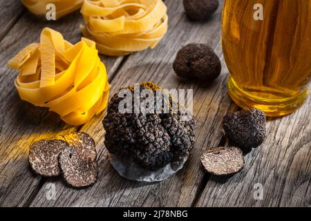 Black edible winter truffle, tagliatelle and fresh basil on wooden table. The most popular cooking ingredients. Stock Photo