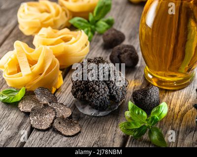 Black edible winter truffle, tagliatelle and fresh basil on wooden table. The most popular cooking ingredients. Stock Photo