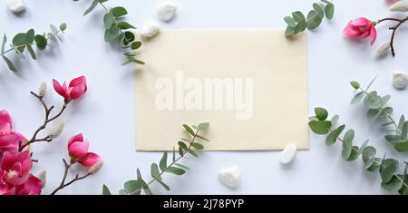 Pink magnolia flowers on twigs, fresh eucalyptus leaves. Blank pink card with grey envelope. Stock Photo