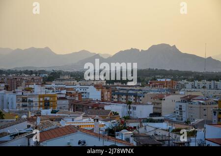 Sunset over the rooftops of Denia, photographed from the Castle, with a view of the mountains in the yellow light on the horizon. Stock Photo