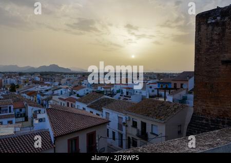 Sunset over the rooftops of Denia, photographed from the Castle, looking at the setting sun between the mountains in the light mist on the horizon. Stock Photo