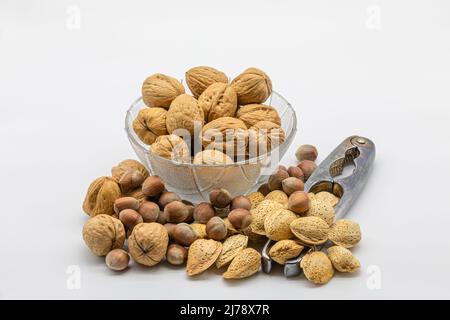 Walnuts, hazelnuts and almonds in a glass bowl with a nutcracker, isolated on a white background Stock Photo