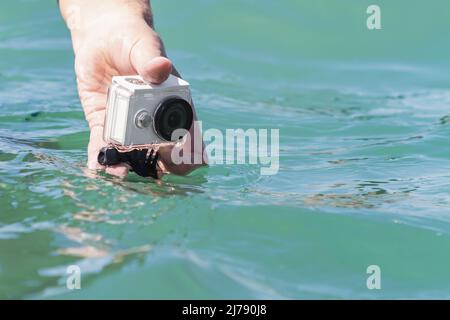 A man is taking photo and video above the water on action camera in underwater case. Closeup, selective focus Stock Photo