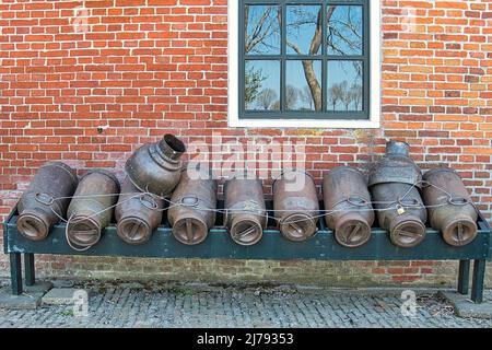 Traditional vintage milk canisters in front of an old farmhouse in the agricultural province of Groningen, Netherlands. Reflection of trees in window Stock Photo