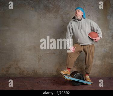 portrait of senior male with one-wheeled electric skateboard in a grunge urban environment Stock Photo
