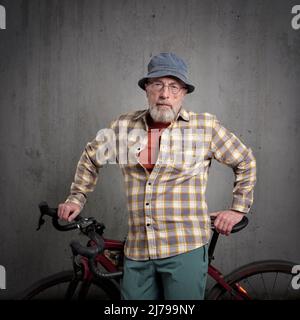 casual portrait of senior male cyclist  with a gravel or touring bike against a grunge concrete wall Stock Photo