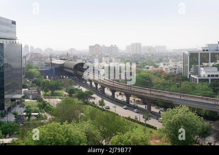 noon shot showing glass covered skyscrapers with offices homes with trees and the elevated metro bridge showing the train public transport in gurgaon Stock Photo