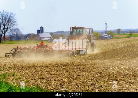 Ronks, PA, USA - April 30, 2022: A farmer uses a tractor to pull a disc harrow to prepare a dry, dusty field for spring planting in rural Lancaster Co
