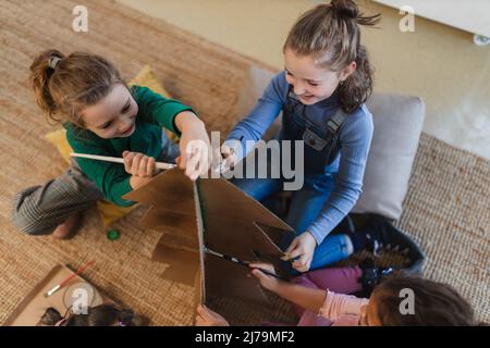 Group of little girls painting cardboard tree at creative art and craft class at school Stock Photo